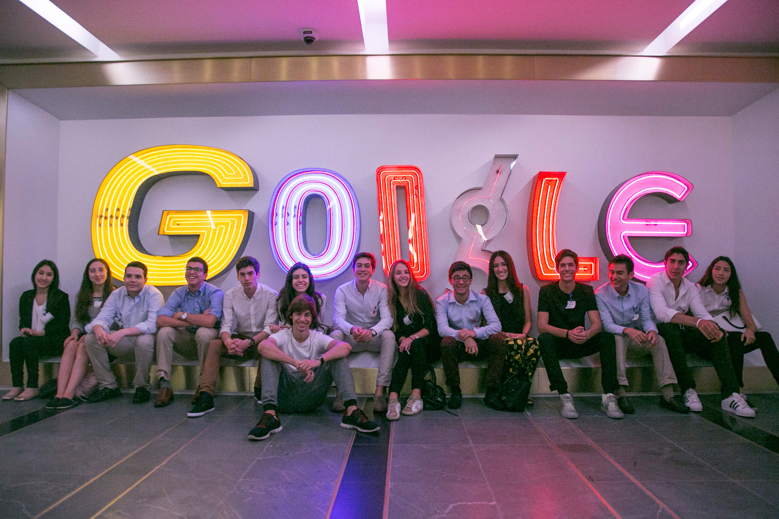 Visionarium students seated beneath giant illuminated Google letters at Google's New York office.