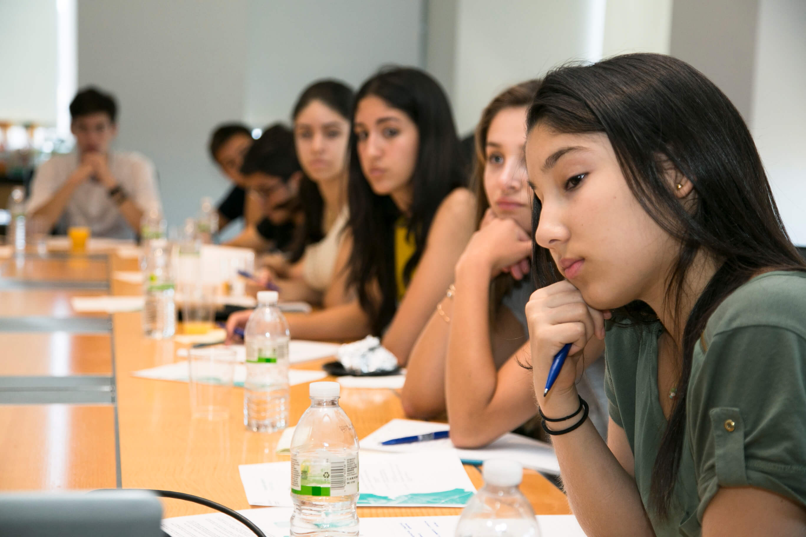 Visionarium students seated along a table in a working session, taking notes and listening.