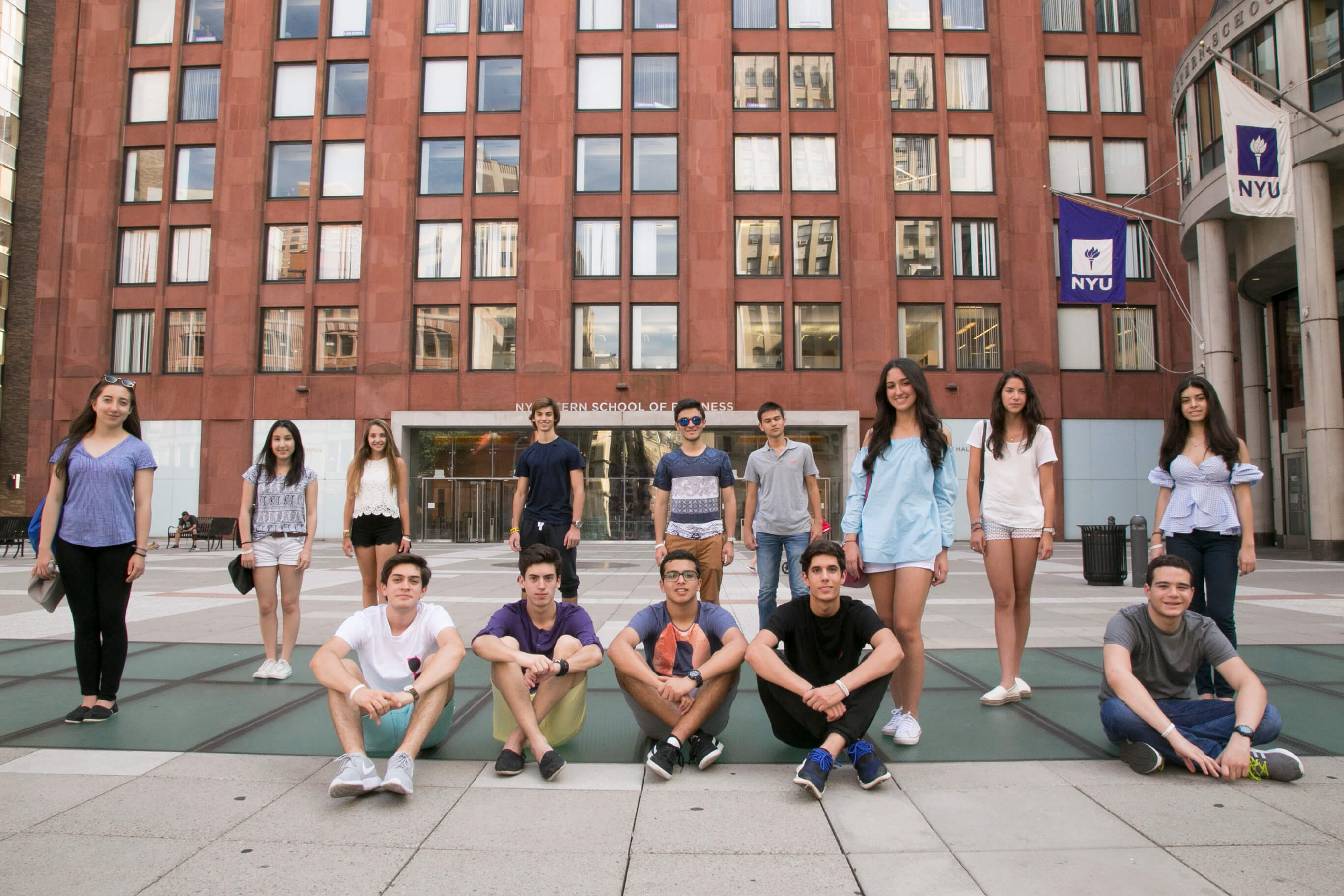 Visionarium students sitting on the plaza in front of an NYU building with purple flags.