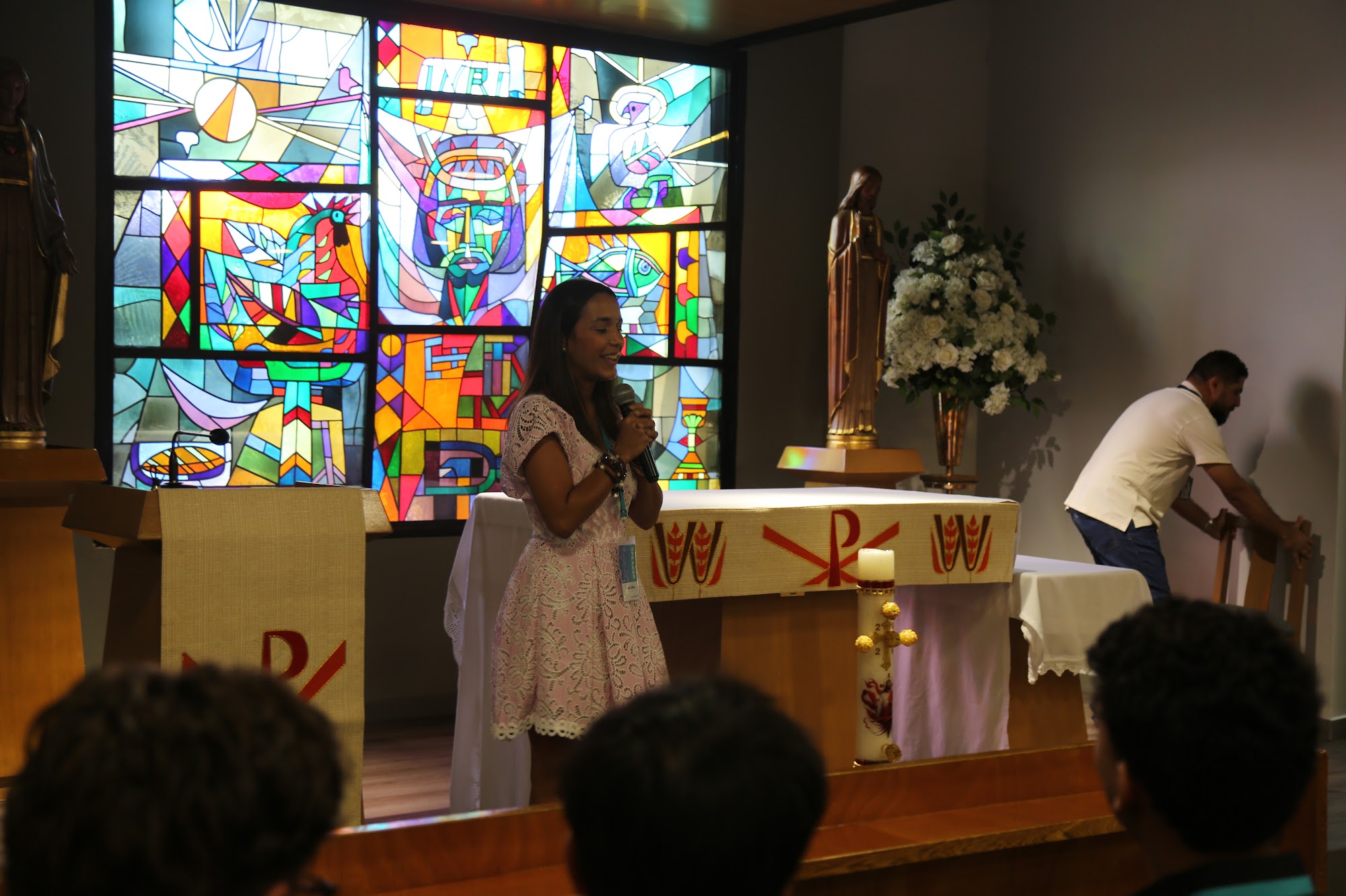A speaker addresses the group from the altar, stained glass behind her.